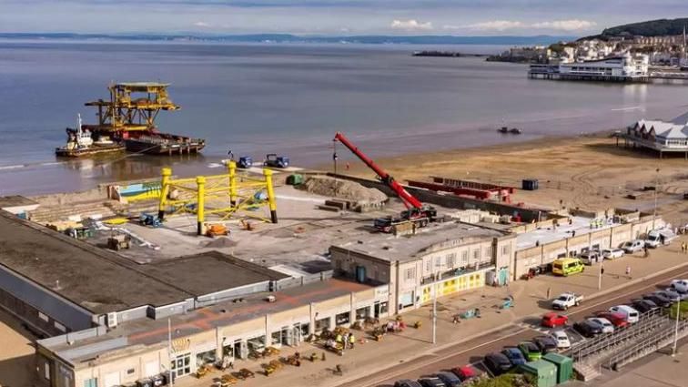 Ariel view of a former North Sea offshore platform being delivered by sea to the Tropicana event venue which is on the beach in Weston-super-Mare. A huge red crane can be seen inside the open air venue.