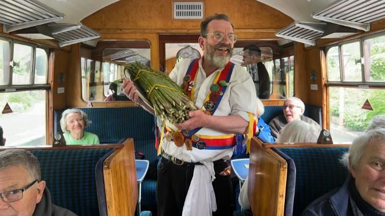 A morris dancer holding a bundle of asparagus