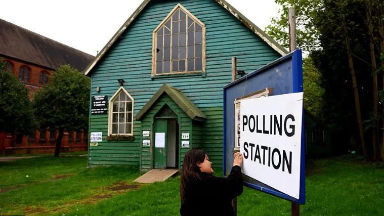 A person standing at a polling station sign
