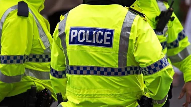 Three police officers in bright yellow fluorescent coats, their faces are not visible 