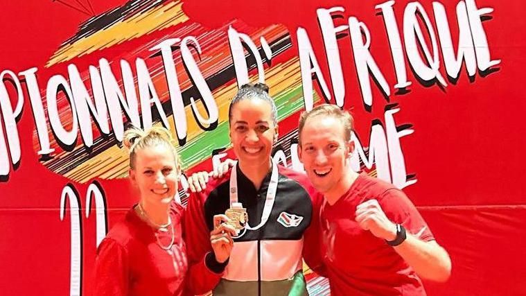 Alexandra Ndolo (middle) holds up her African fencing gold medal with a person celebrating either side of her