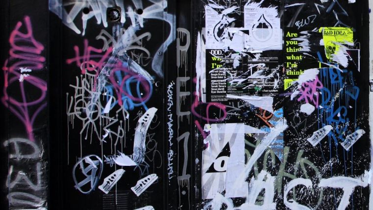 Image shows black wall covered in graffiti and posters. 