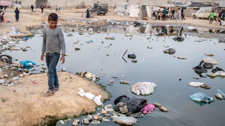 Palestinian boy walks next to pool of sewage water with rubbish inside in Rafah on 26 April 2024