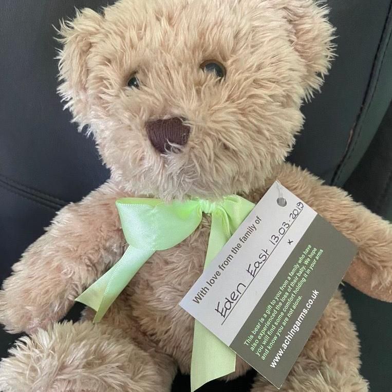 A small beige teddy bear wearing a green ribon tie