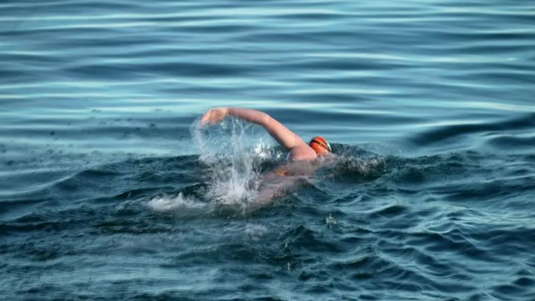 A young girl with an orange swimming cap doing front crawl in the sea.