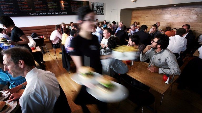 Waitress carries burgers past diners in a busy branch of the burger restaurant GBK