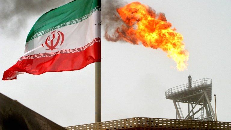 A gas flare on an oil production platform in the Soroush oil fields is seen alongside an Iranian flag in the Persian Gulf, Iran, in July 2005