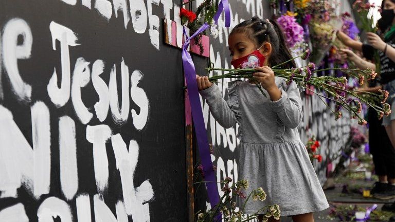 A girl places flowers beside the names of victims of femicide in Mexico on fences placed outside the National Palace ahead of a Women"s Day protest in Mexico City, Mexico March 7, 2021