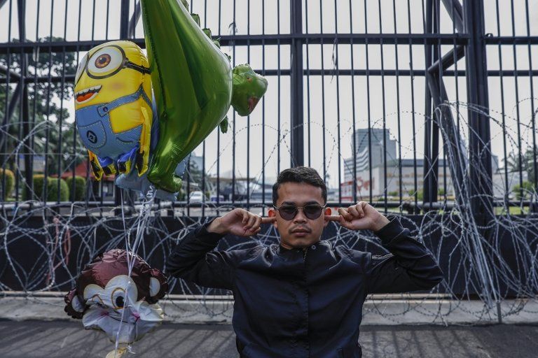 A protester covers his ears as he sits in front of the main gate of the parliament building during a protest in Jakarta