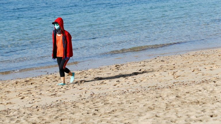 A woman wearing a face mask walks on a beach in Lanzarote