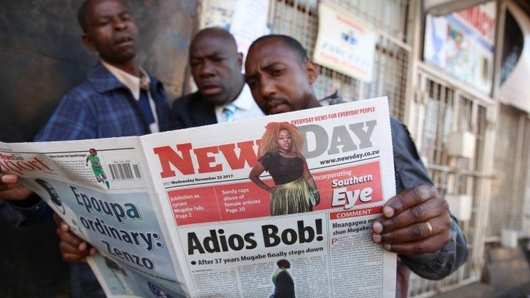 People read a newspaper on a street in Harare, Zimbabwe, 22 November 2017