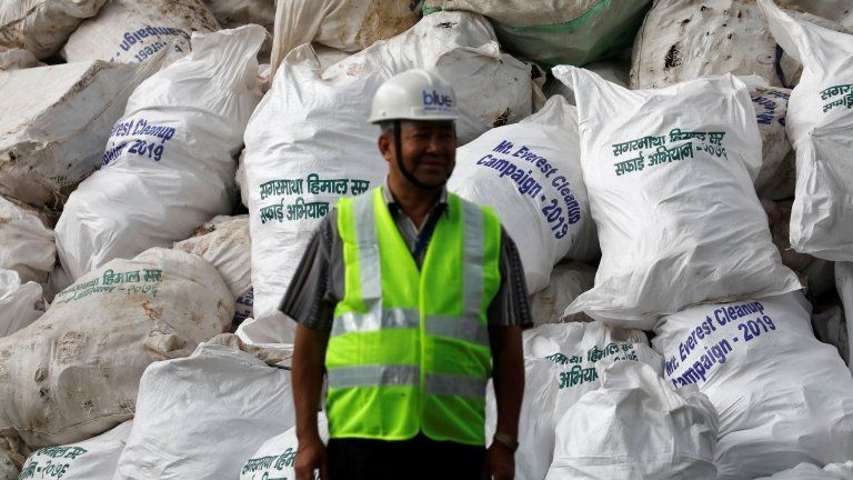 A man stands in front of piles of rubbish collected as part of the Mount Everest Cleanup Campaign in 2019