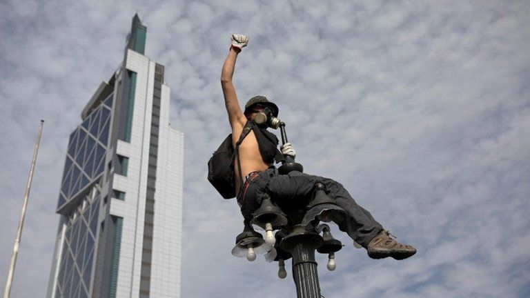 A demonstrator sits on a street light as protests against high living costs continue, in Santiago, Chile October 22, 2019