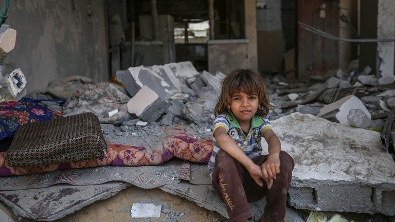 A Palestinian child sits in the rubble of their home
