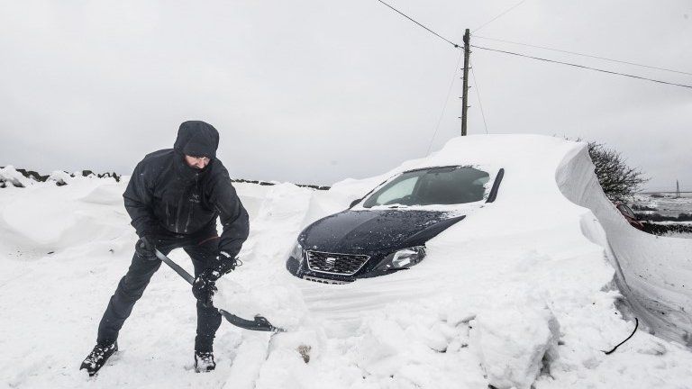 A man digs out a car stuck in snow in Ripponden, Yorkshire