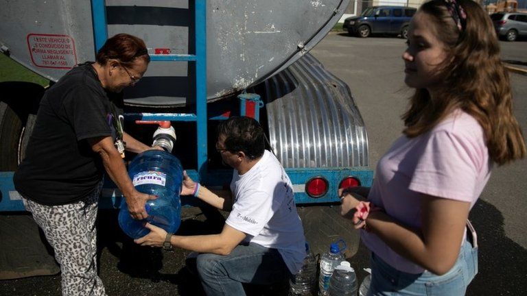 People get containers filled with water from a water tank truck