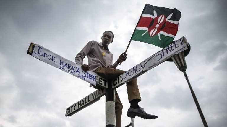 A supporter of The National Super Alliance (NASA) opposition coalition and its presidential candidate Raila Odinga sits on top of a street sign post that has been relabeled "Judge Maraga Street", referring to Chief Justice David Maraga,