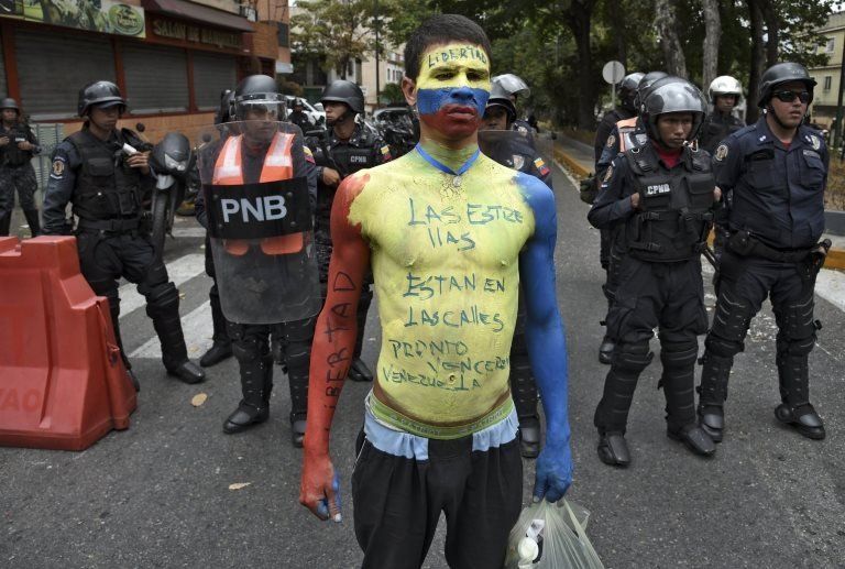 A man with his body painted in the Venezuelan national flag"' colours reading "The stars are in the streets. We will soon be victorious Venezuela", demonstrates in front of riot police during an opposition demo near La Carlota Air Base in Caracas on May 4, 2019
