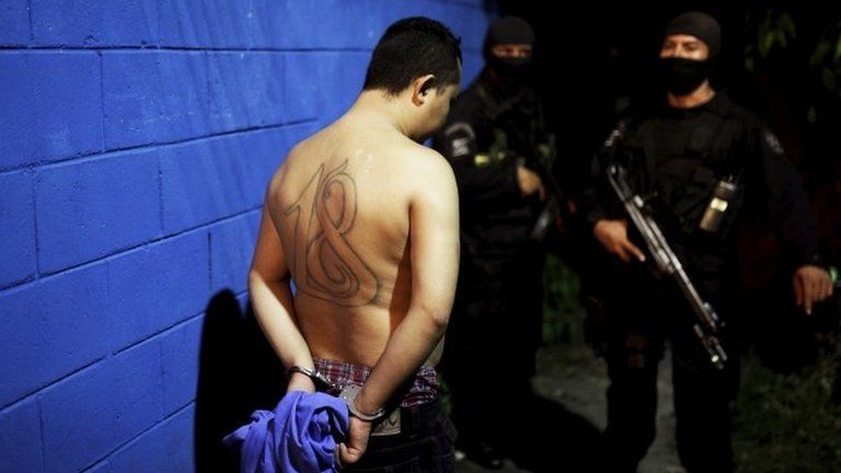 A member of the 18th Street gang is guarded by policemen after he was arrested as a suspect of ordering a public transportation service in San Salvador on 28 July, 2015.