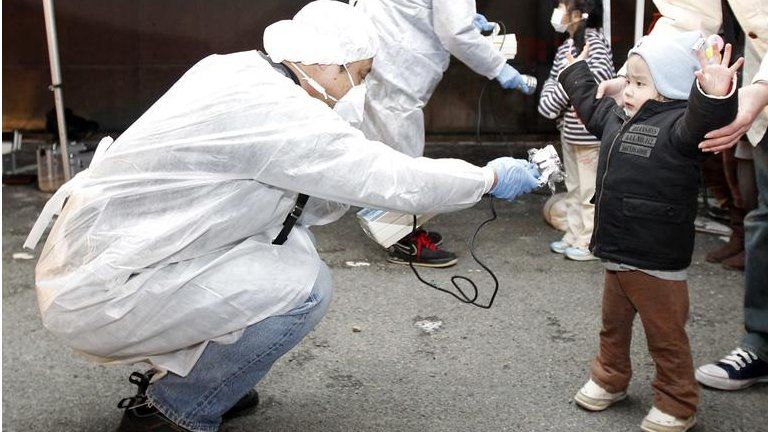 Officials in protective gear check for signs of radiation on children who are from the evacuation area near the Fukushima Daini nuclear plant in Koriyama, on 13 March 2011