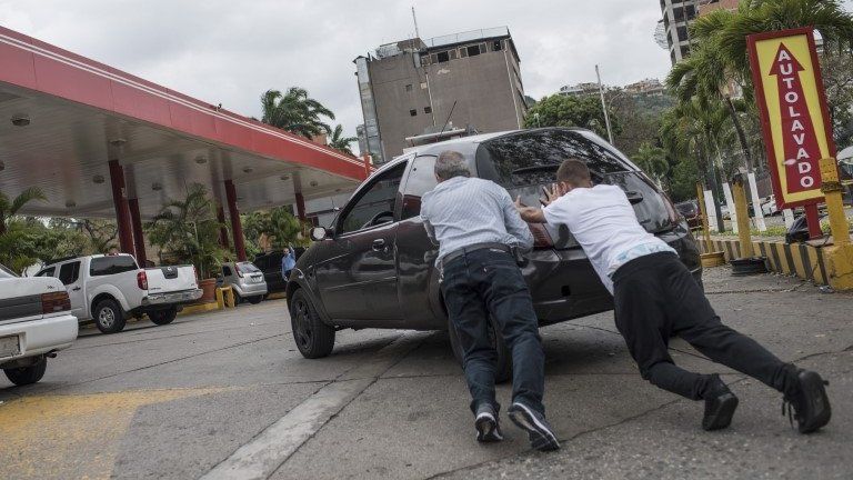 Two men push a car into a gas station in Caracas on March 23, 2017