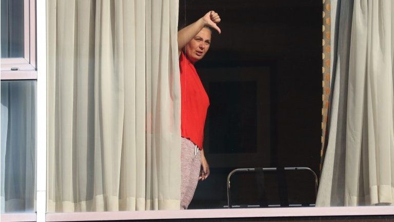 A woman gives a thumbs down gesture to members of the media from the window of Radisson Blu Edwardian Hotel, near Heathrow Airport