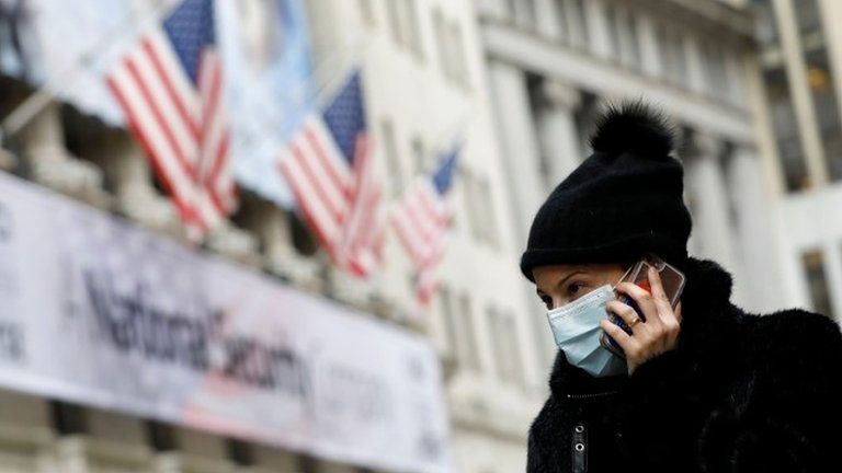 A woman in a surgical mask uses her mobile phone in New York