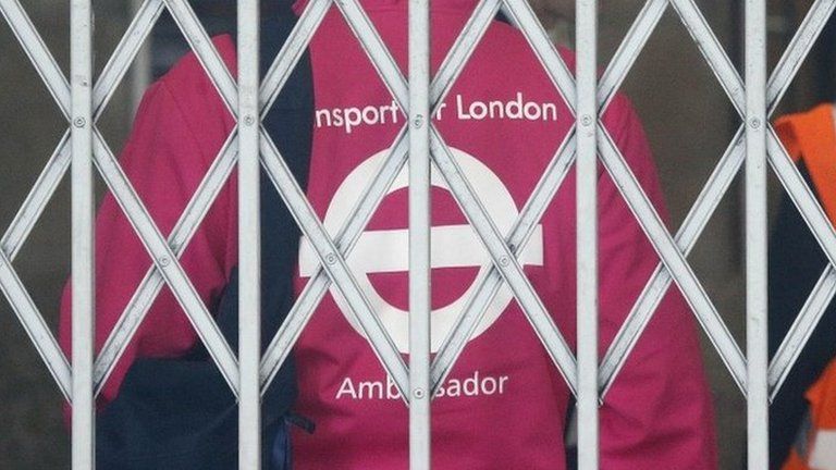 A transport assistant waits behind the fence of the closed tube station at Victoria as tube drivers are on strike in London