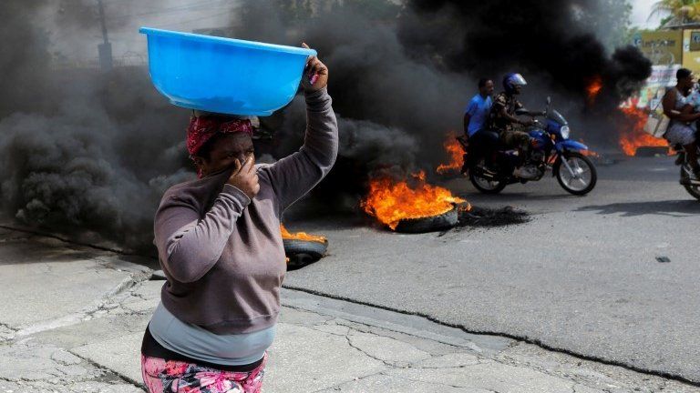 A woman covers her nose while walking past a burning road block as anger mounted over fuel shortages that have intensified as a result of gang violence, in Port-au-Prince, Haiti, July 13, 2022.