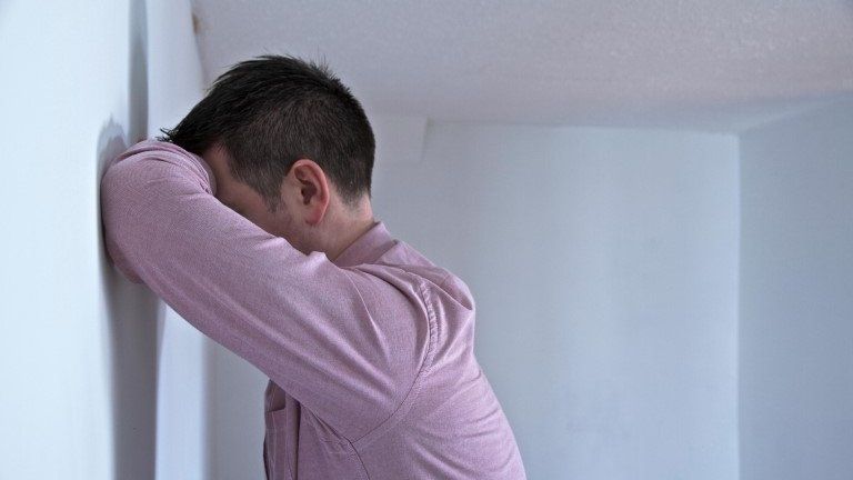 Man leans on wall with his face resting on his arm