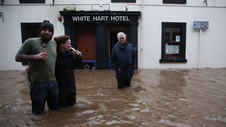 People wade through the water to get to the White Hart Hotel as the River Nith bursts its banks in Dumfries