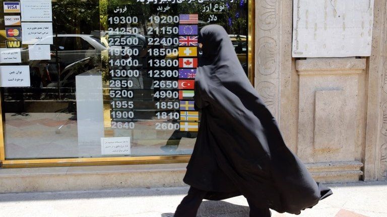 An Iranian woman checks the currency rate as she walks past a currency exchange service in Tehran, Iran, 22 June 2020