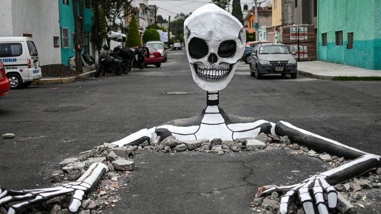 A huge cardboard cardboard skeleton emerges from a street in Mexico City