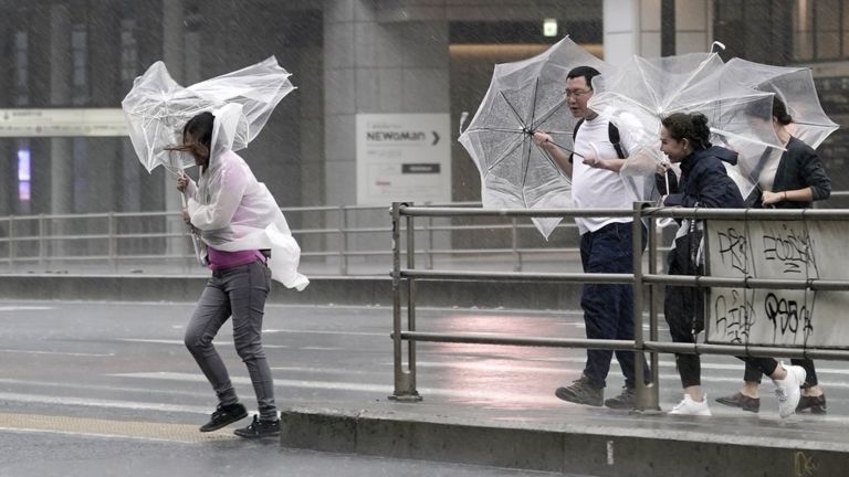 Pedestrians in Tokyo struggle with umbrellas in the wind and rain
