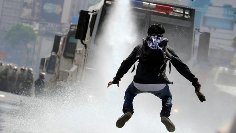 A demonstrator jumps away from a jet of water released from a riot security forces vehicle during a rally against Venezuela"s President Nicolas Maduro in Caracas, Venezuela, May 26, 2017.