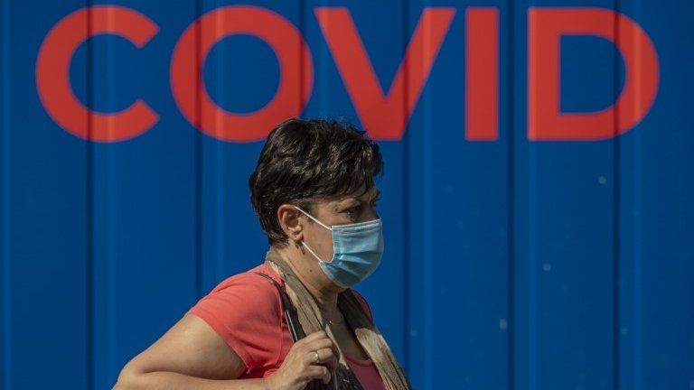 A woman wearing protective face mask walks in front of a coronavirus testing station