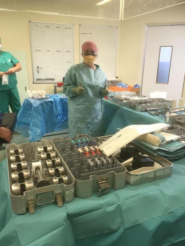 Yoana viste una bata verde completa en un quirófano, rodeada de utensilios utilizados en prótesis articulares.