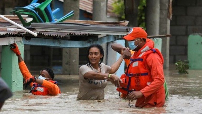 Members of the Civil Defence help a woman in a flooded street after the passage of Storm Laura, in Azua, Dominican Republic August 23, 2020.