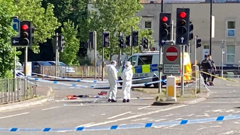 Stapleton Road near the scene of the incident. People wearing white forensics suits can be seen in the foreground, with uniformed police officers and a van to the rear of the image.  