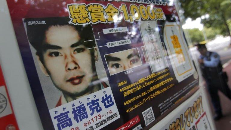 A police officer walks near a wanted poster of former Aum Shinrikyo cult member Katsuya Takahashi displayed at the metropolitan police department in Tokyo, Sunday, June 10, 2012
