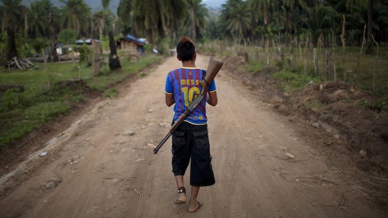 A boy with a rifle slung over his back, patrols an area of La Confianza, Honduras - May 2012