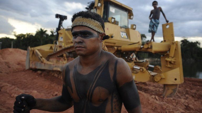 Brazilian indigenous man next to heavy machinery