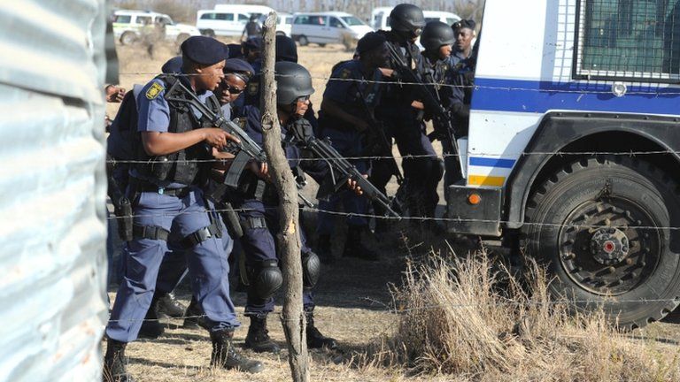 Police officers look at protesting miners near a platinum mine in Marikana on 16 August 2012