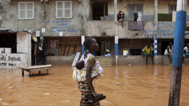 A woman with a baby on her back wades through water after overnight flooding on a street in Senegal's capital Dakar, August 14, 2012
