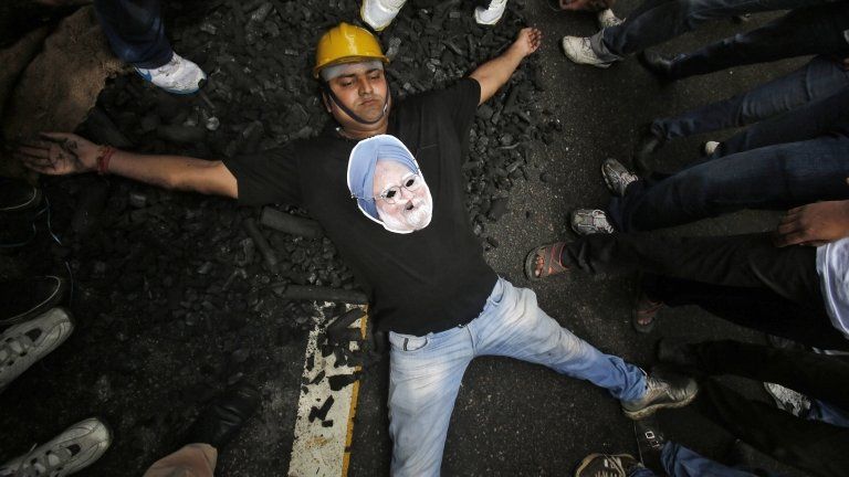 An activist from Bharatiya Janata Yuva Morcha, wearing a cut-out of India's Prime Minister Manmohan Singh, lies on a heap of charcoal during a protest in New Delhi August 29, 2012.