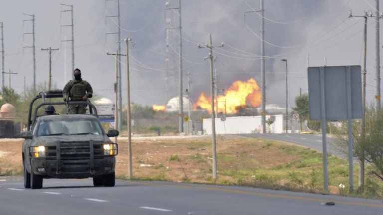 A Mexican army vehicle patrols on a road as fire and smoke rise from a gas pipeline distribution centre in Reynosa, Mexico near Mexico"s border with the United States, Tuesday Sept. 18, 2012