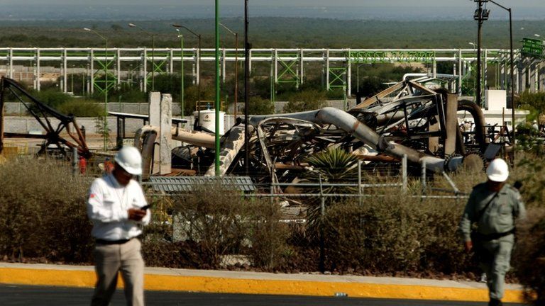 Workers walk past burnt-out parts of Pemex gas plant