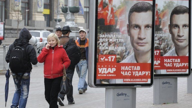 People walk past election posters of Ukrainian boxer and Chairman of the Ukrainian UDAR Party, Vitali Klitschko in Kiev, Ukraine, Thursday, Oct. 18, 2012