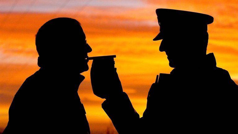 Silhouetted motorist gives a breath test to a police officer