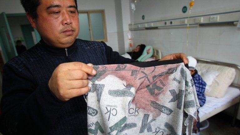 A man displays his son's bloodstained coat in Guangshan, Henan, on 16 December 2012